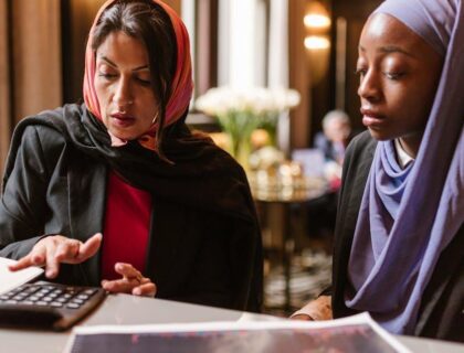 Two multicultural women collaborating on financial analysis using a calculator.